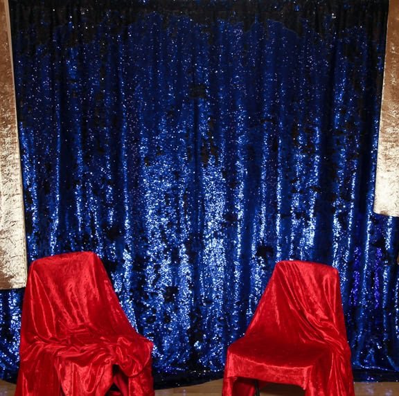 Stylish photo booth with blue sequin backdrop and red chairs for events.