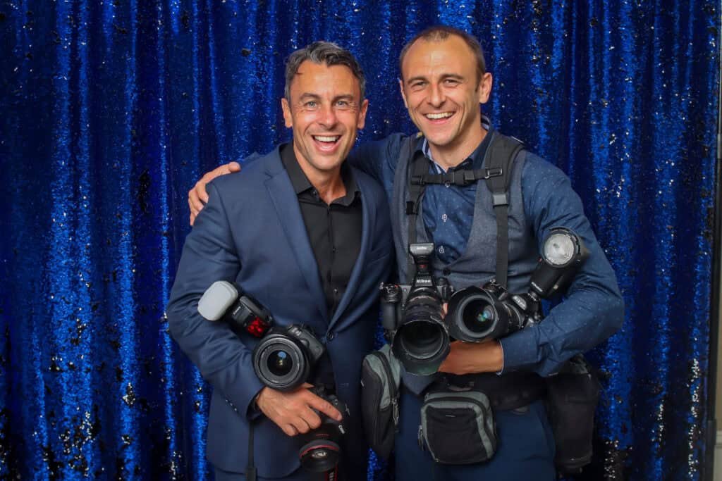 Photographers with professional cameras smiling against a sparkling blue backdrop.