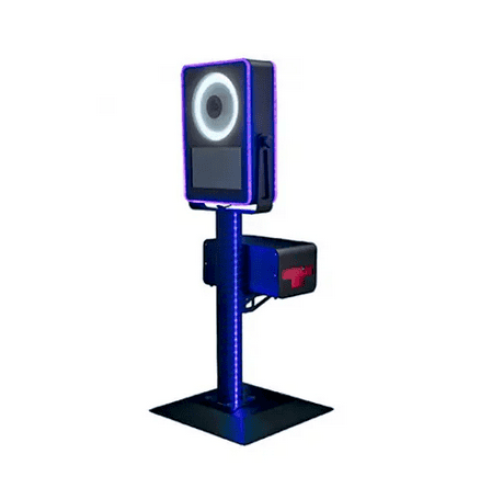 A modern photo booth machine with a ring light, screen, and camera on a tall stand; equipped with LED lighting and a rectangular compartment attached to the side.