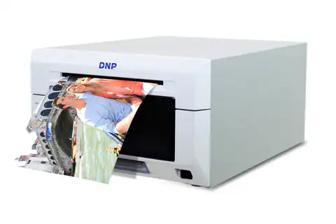 A white DNP photo printer is printing a color photograph showing three people smiling in a boat on water, with buildings visible in the background.