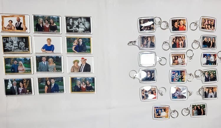 A collection of rectangular and square photo keyrings and magnets arranged on a white surface, each displaying various groups of people posing together at what appears to be a formal event.