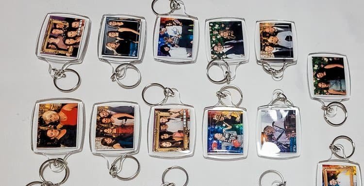 A collection of rectangular keyrings, each containing a small group photo of people, is spread out on a white surface. The keyrings have metal rings attached.