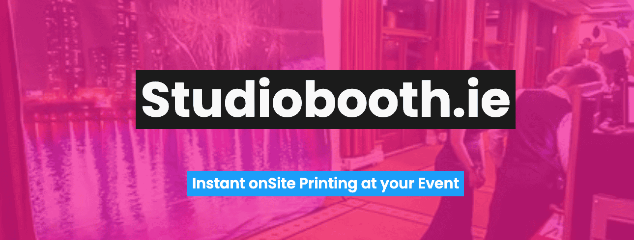 A pink-tinted image with the text “Studiobooth.ie” in bold white letters and “Instant on-site Printing at your Event” below; people interact near a photo booth, with city lights visible through windows.